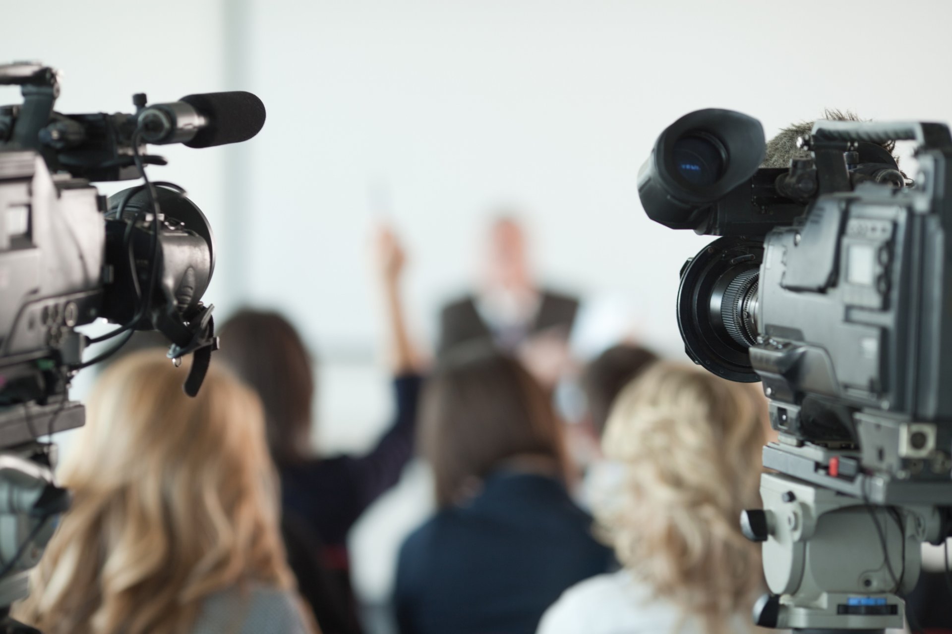 Video cameras pointed at businessman or lecturer giving a presentation in background. Focus on cameras.